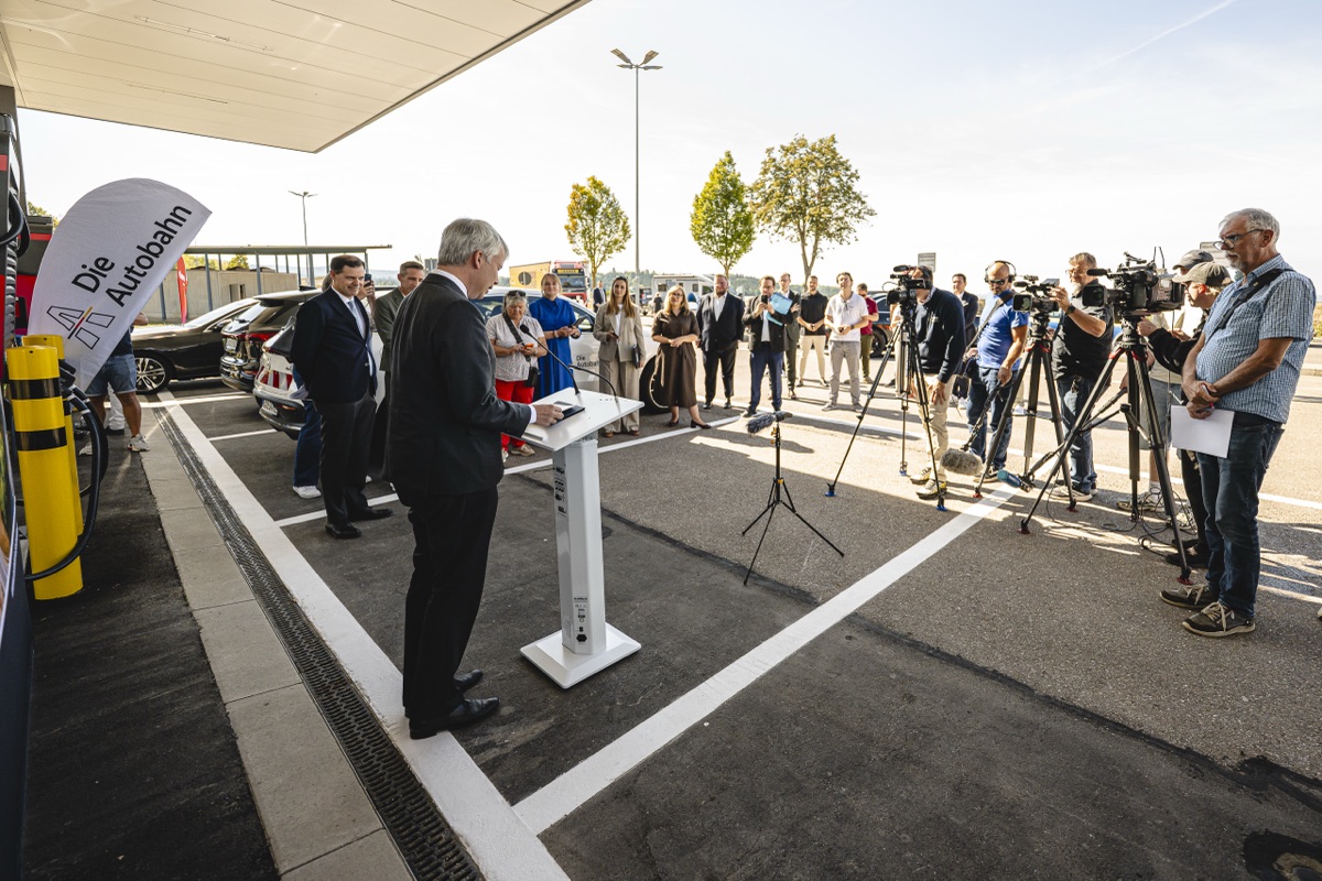 Rede am Pult, gegenüber Kamerateams, Fotografen und Gäste