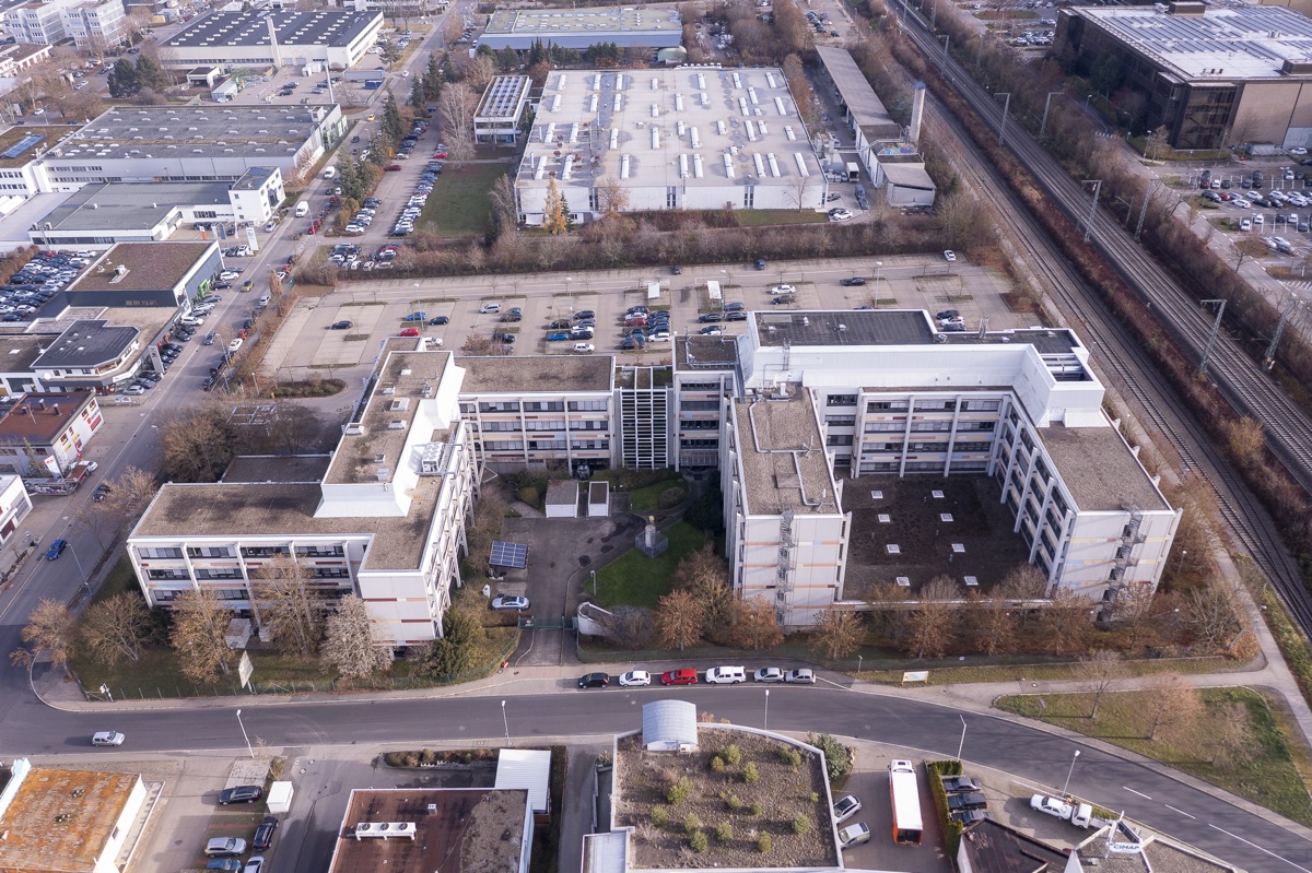 Bürocampus aus der Luft, Winter: mehrere Gebäude, Parkplätze, Bahngleis