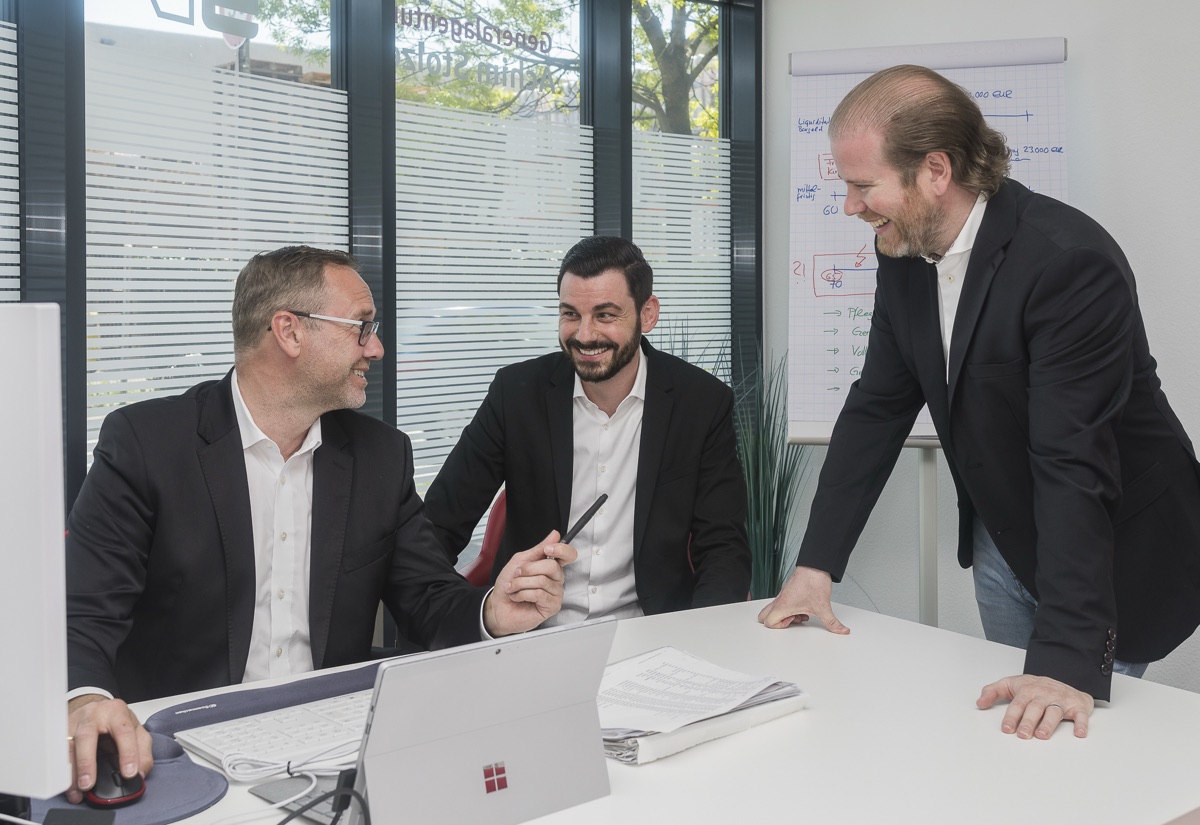 Besprechung im Büro, drei Kollegen im Gespräch am Schreibtisch