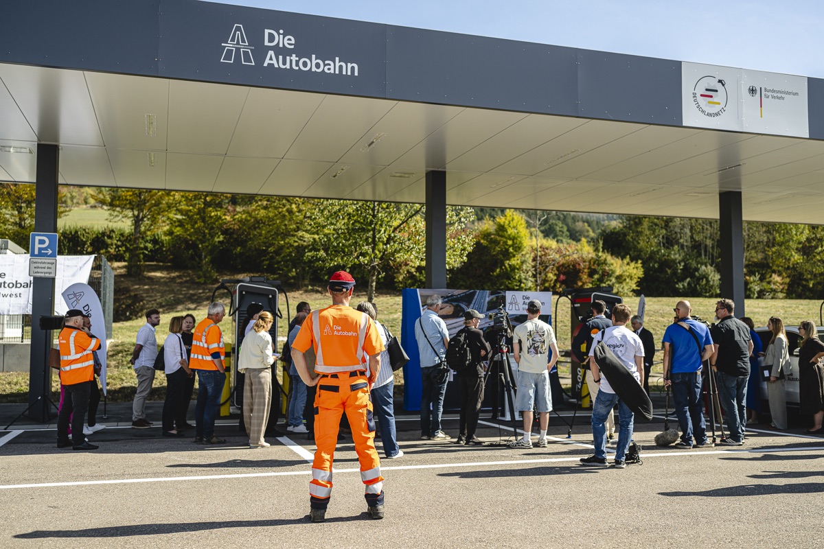 Pressetermin am Schnellladestandort: Mitarbeiter in Warnkleidung, Gäste und Presse unter dem Ladedach